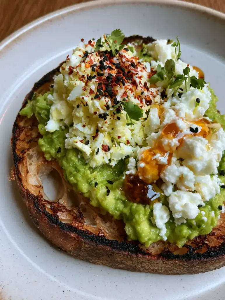 Detailed shot of amber-colored hot honey drizzling over creamy white feta on a slice of gourmet avocado toast.