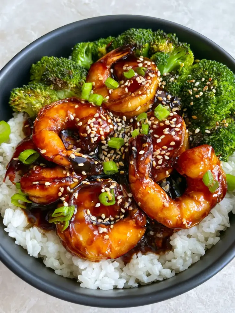 Close-up of golden-brown seared jumbo shrimp coated in a mahogany teriyaki glaze in a charcoal bowl.