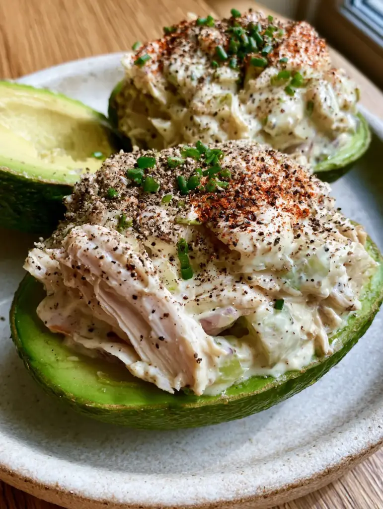 Handheld photo of a stuffed avocado half with a scoop removed to show the buttery fruit texture.