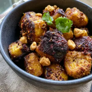 Macro close-up of Kelewele plantain cubes with a grainy ginger-clove coating and charred edges.