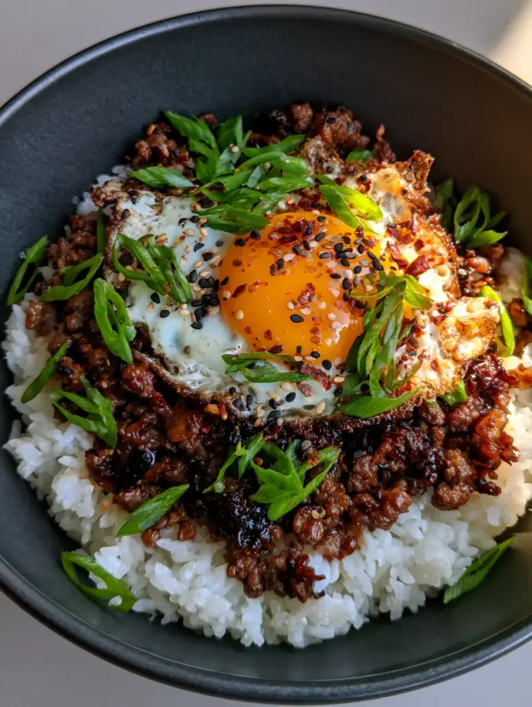 Close-up of the mahogany soy glaze on seared ground beef with a garnish of black and white sesame seeds and scallions.