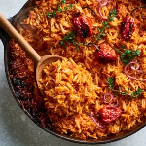 Close-up of Cameroonian Jollof Rice grains coated in vibrant orange-red spicy tomato oil with fresh thyme.